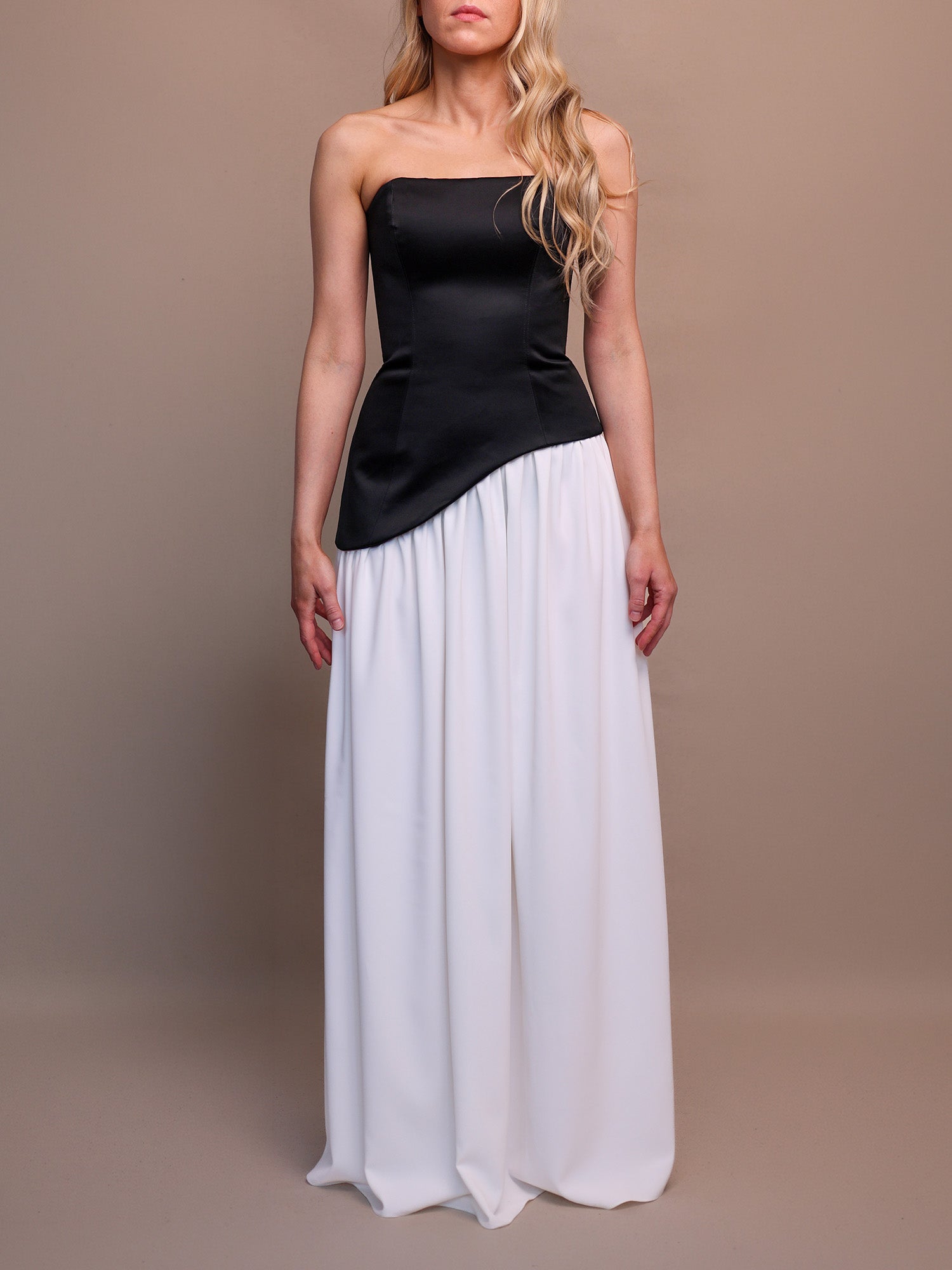 Woman wearing a black and white strapless gown with with asymmetric hemline on a brown background. 