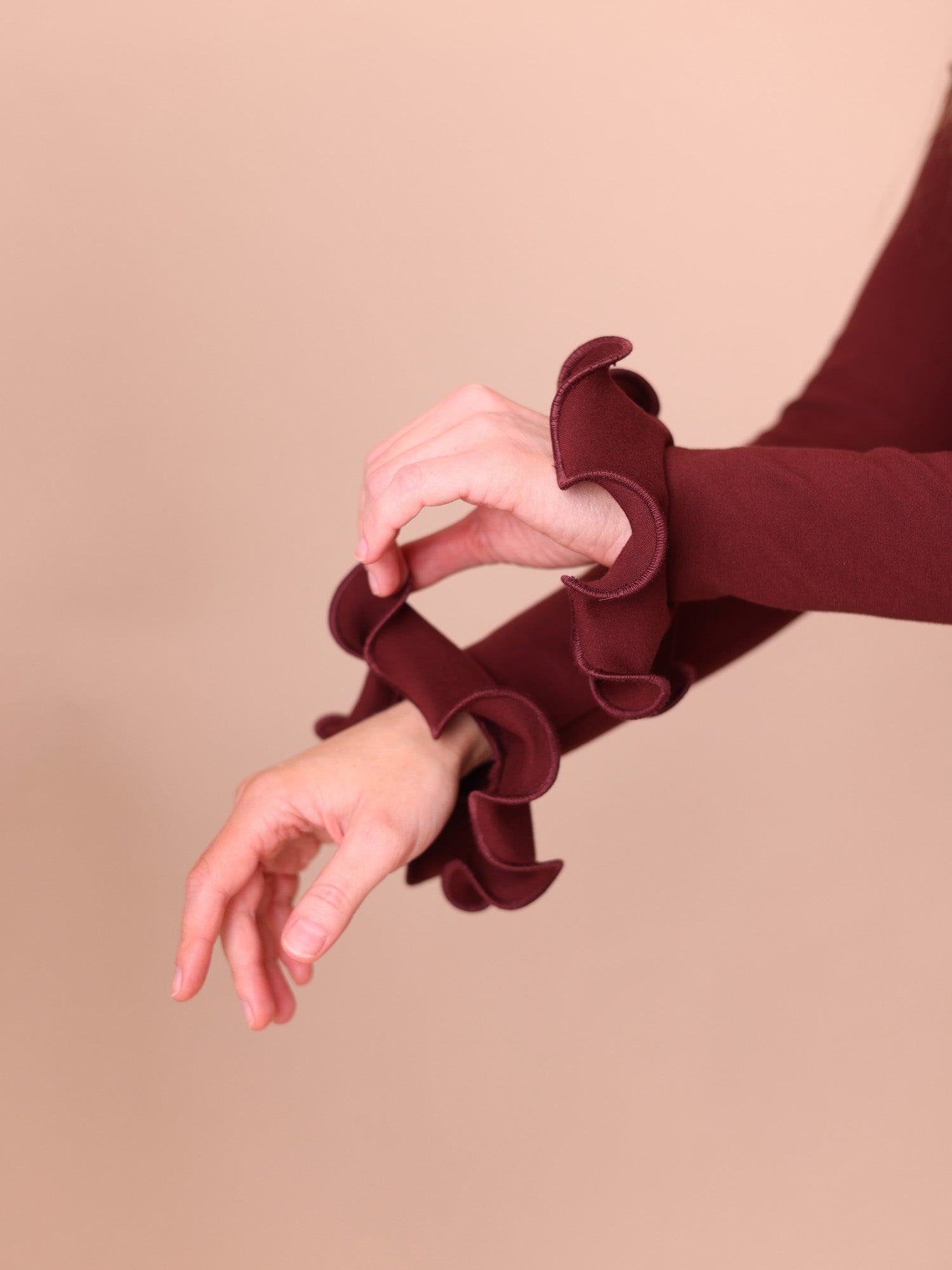 Close-up of a burgundy sleeve with ruffled cuffs on a beige background