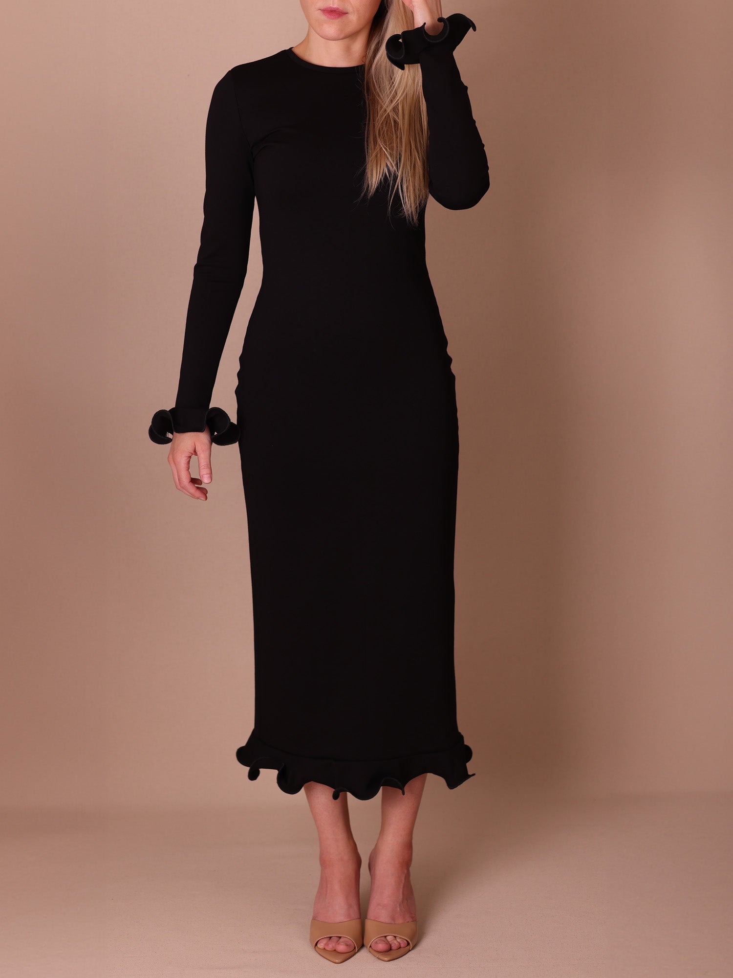 Black long-sleeve dress with flower cuffs and flounced hem worn by a person on a beige background.