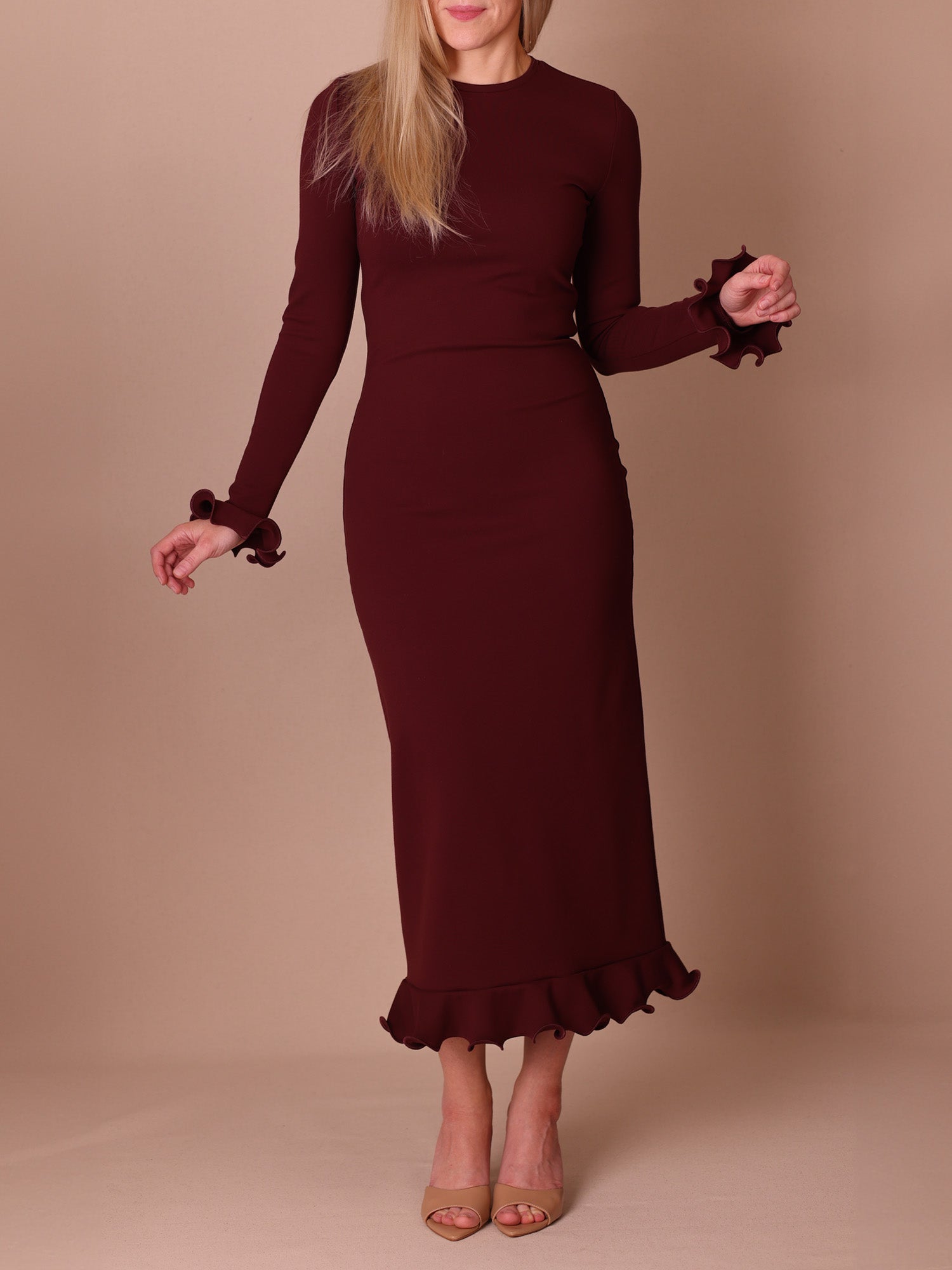 Woman wearing a burgundy dress with ruffled sleeves and hem against a beige background