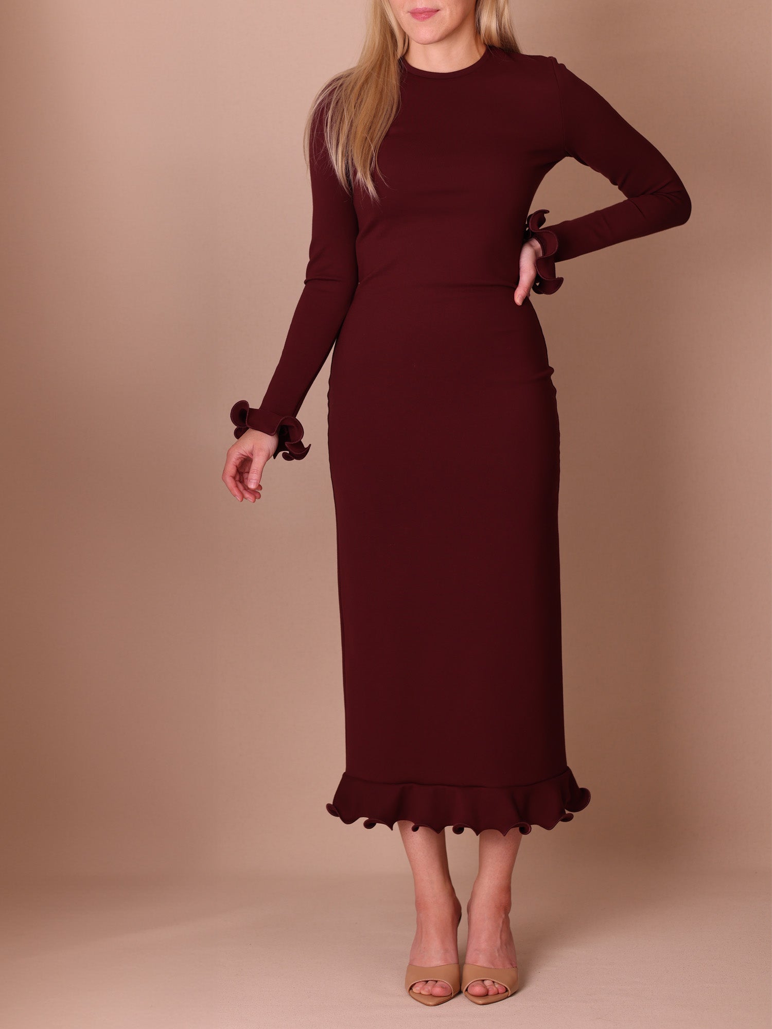 Woman wearing a burgundy dress with ruffled hem and with flounced cuffs against a beige background