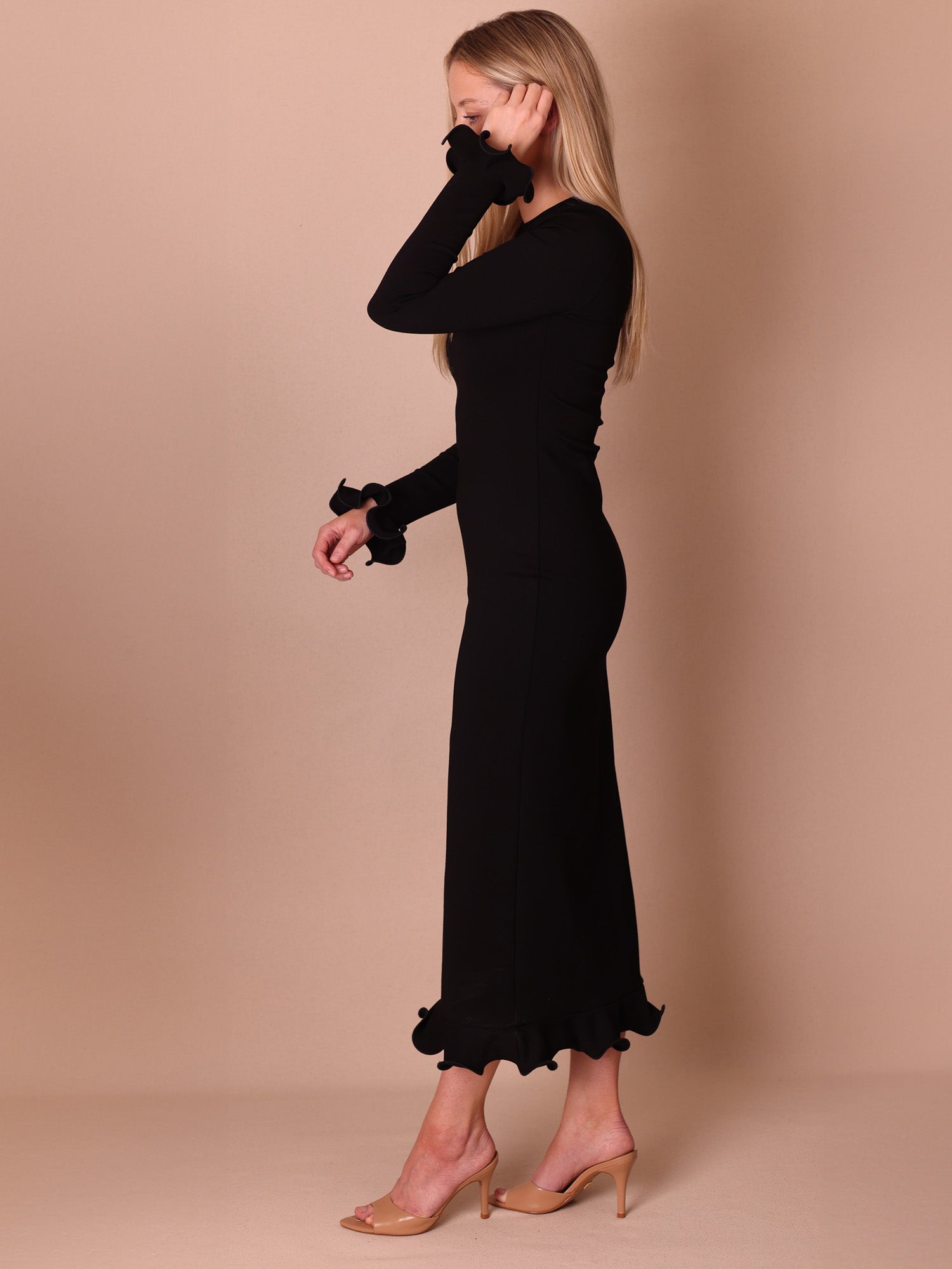 Woman wearing a black dress with ruffled sleeves and hem against a beige background