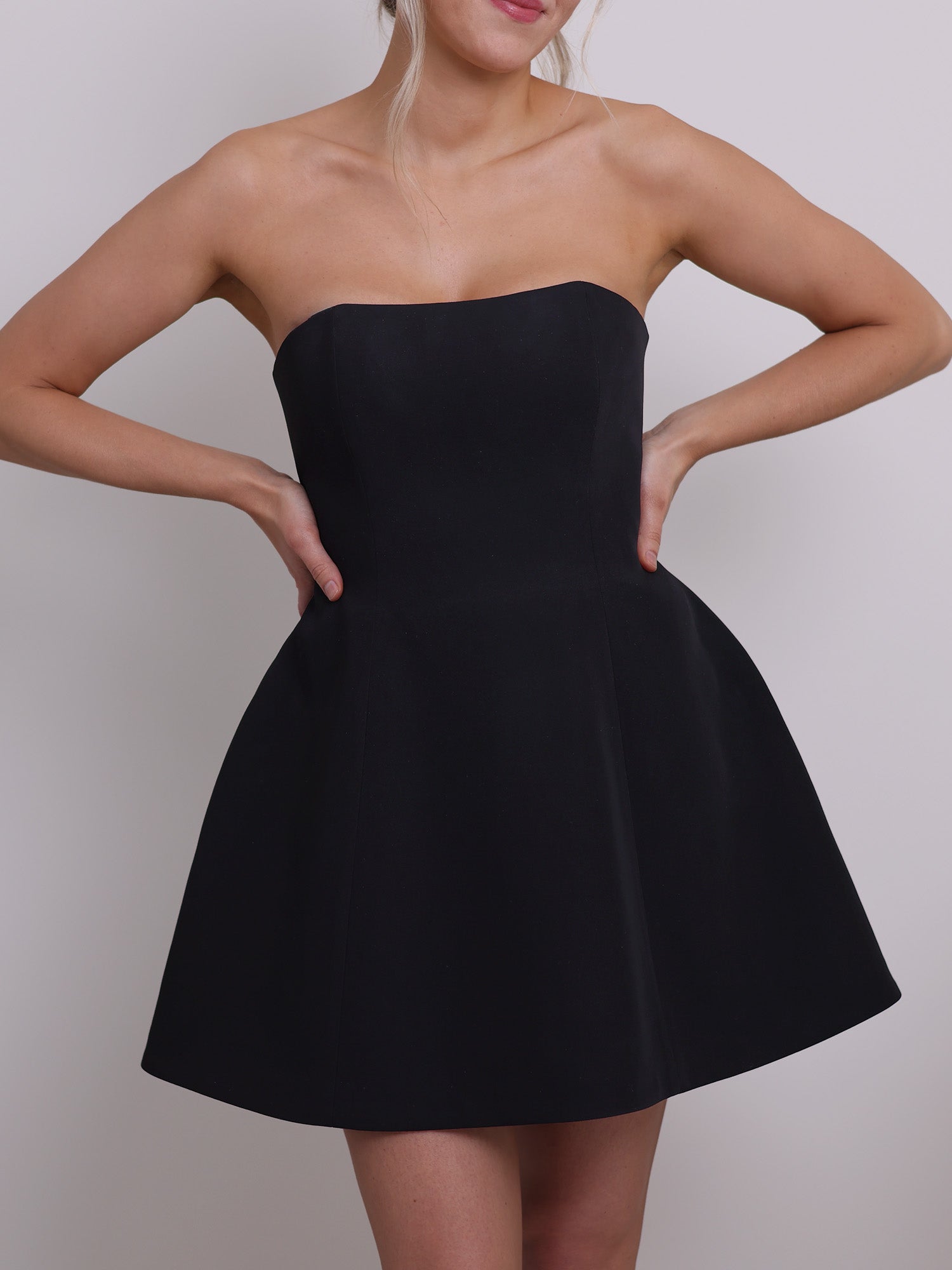 Front view of a strapless mini corset dress sewing pattern, showcasing an hourglass silhouette with a structured, boned bodice and flared bell-shaped skirt in black fabric.